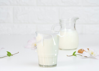 full glass cup of fresh milk with splashes stands on a white table, healthy breakfast