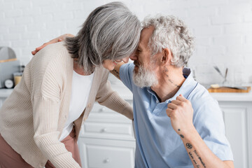 Fototapeta premium Mature man hugging smiling wife in kitchen.