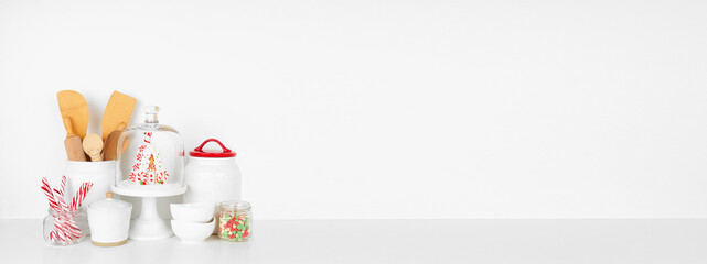 Christmas theme kitchenware and sweets on a white shelf or counter. Banner against a white wall background with copy space.