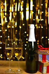 Glasses of champagne on golden background with christmas gifts on wooden table