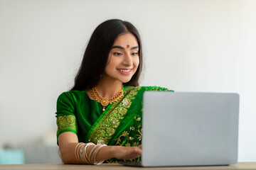Millennial Indian lady in stylish sari dress studying or working online, using laptop at home