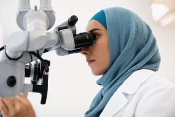 Female Dentist Doctor In Hijab Working With Modern Dental Microscope In Clinic