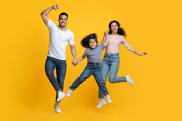 Crazy Offer. Funny Arab Family With Little Daughter Jumping Over Yellow Background