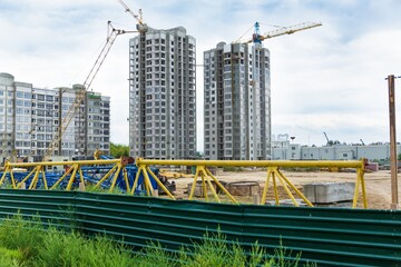 Large construction site including several cranes working on a building complex, with clear blue sky and the sun