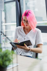 tattooed businesswoman with pink hair writing on notebook.