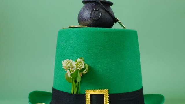 Saint Patrick festive background.Black bowler hat with coins on a green leprechaun hat and a bunch of clovers with gold coins on a light green background. 4k footage