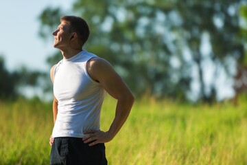 Successful man raising arms after cross track running on summer sunset. Fitness male athlete with arms up celebrating success and goals after sport exercising and working out.