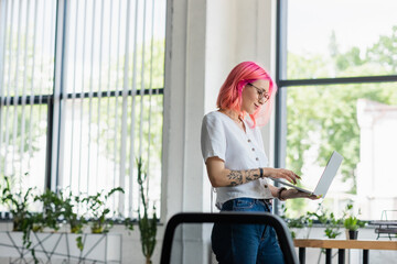 Fototapeta na wymiar happy young businesswoman with pink hair using laptop in office.