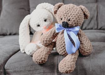 knitted teddy bear and rabbit sitting and talking on a sofa. hand made kids gifts, hobby for meditation and relaxation.