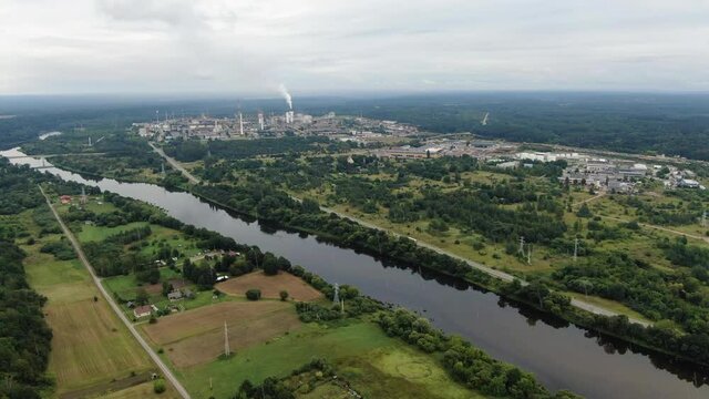 Cityscape of Jonava and chemical industry buildings with smoking chimneys in horizon during light rainstorm, aerial drone view
