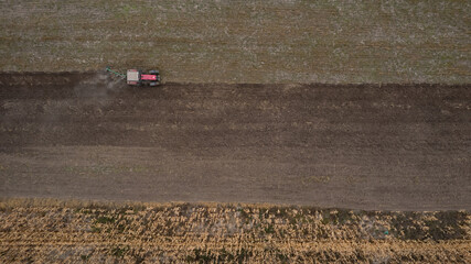 Fototapeta na wymiar Red Tractor Plowing in Autumn near corn field. Top view from drone