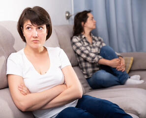 Portrait of sad mature female sitting at sofa after quarrel quarrel, woman on background