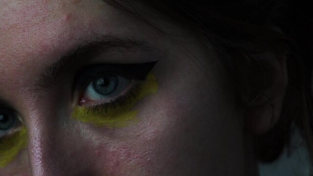 Close up on a woman's blue eyes, with yellow makeup in cyberpunk style. Young looking eyes with black eyeliner and yellow watercolor paint. Vague fantasy.