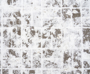 Snowy street tiles texture. Stone masonry on the pavement. Footprint in the snow from a boot