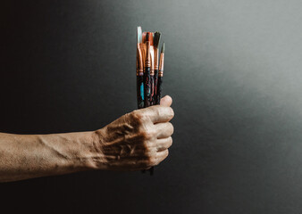 Studio dark tones image of a old hand grabbing a painting palette and painting brush, artistic...