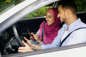 Young Muslim Spouses Riding Car And Using Smartphone Together, Through Window Shot