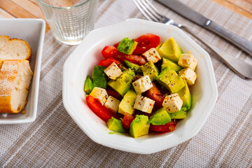 Traditional Mediterranean style salad from fresh ripe avocado with tomatoes and soft feta cheese seasoned with aromatic dried herbs and olive oil