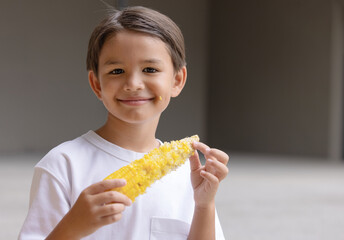 A cute boy smiling and holding corn on the cob