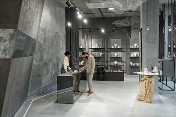 Interior of jewelry boutique with male buyer and shop assistant standing by display with assortment...
