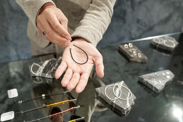 Hands of young man holding handmade bracelet over his palm while showing it to consumer in jewelry...