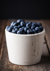 Blueberries in white ceramic bowl on rustic wooden background. Selective focus. Shallow depth of field.