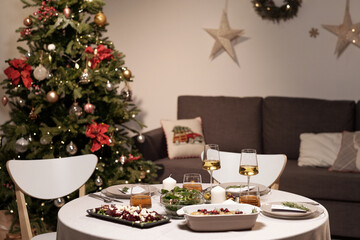Round table served for festive family dinner on background of decorated xmas tree and couch with cushions in living-room