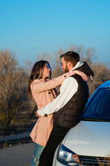 Young couple in love looks at each other and hugs outdoors. Lovers in casual style stand near car. Lifestyle, youth and adventure concept