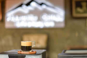 A clear cup of coffee is placed on a brown lacquered wooden surface