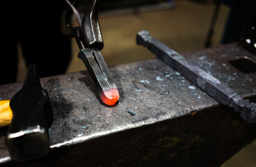 A glowing piece of metal on an anvil held by a pair of metal tongs