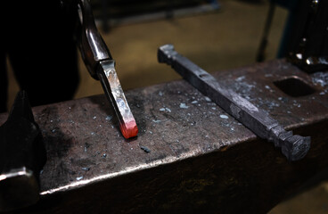 A glowing piece of metal on an anvil held by a pair of metal tongs