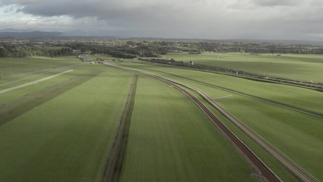 Green aerial flyover of horse race track under overcast Irish sky