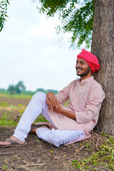 Young indian farmer sitting at agriculture field.