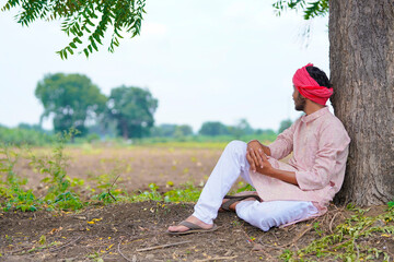 Young indian farmer sitting at agriculture field.