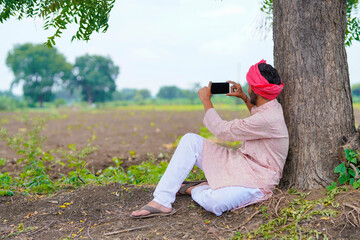 Indian farmer sitting at agriculture field and using smartphone.