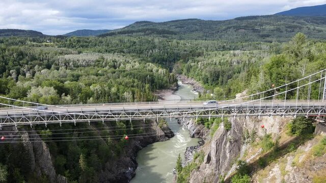 4k aerial footage filmed in 30fps approaching and flying over an old Canyon bridge in remote British Columbia. Few cars crossing the skeena river on sunny day in the northern Rocky Mountains.