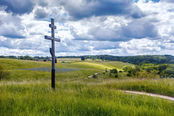 Fototapeta na wymiar The wooden orthodox cross with the green fields on the background