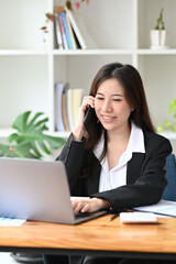 Fototapeta na wymiar Smiling businesswoman using laptop computer and talking on mobile phone.