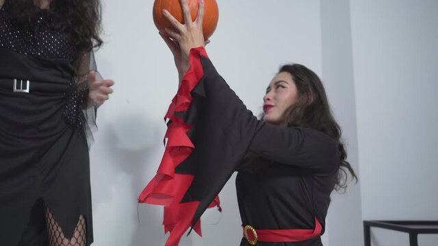 Funny Pretty Ladies In Halloween Witch Costumes Playing With Witch's Broom And Pumpkin In The Bedroom. tilt-up