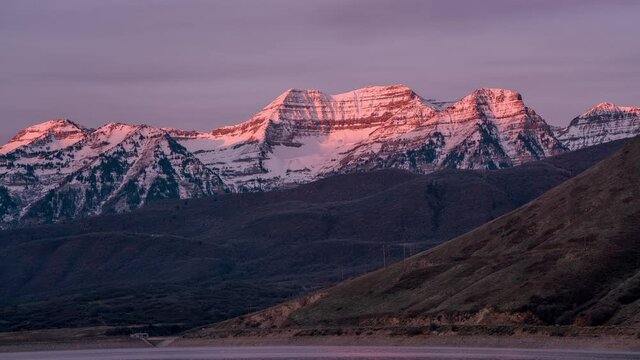 Time lapse of the sun lighting up the snow capped mountain at sunrise viewing Timpanogos Mountain from Deer Creek Reservoir in Utah.