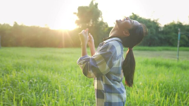 A happy successful female farmer  celebrating herself with cheerfully dance with raising fists up while standing against on a growth green crops field and beautiful golden sunset, excited celebrating 