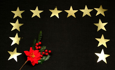 Red Mexican poinsettia flowers to frame Christmas message on black background with golden stars, canes, handmade doll
