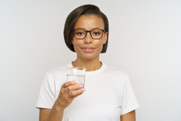 Young female in glasses with glass of pure water. African american woman training healthy habits of drinking water in morning and during day to keep hydration balance, weight and healthcare concept