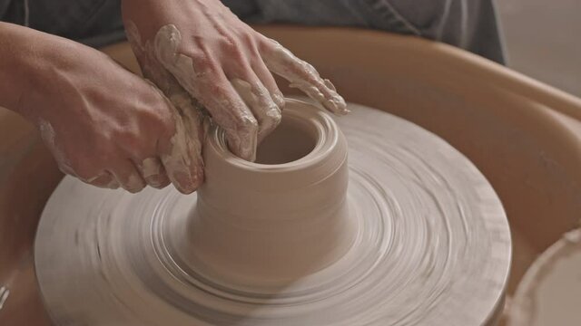 PAN close-up of unrecognizable female hands working with clay on pottery wheel at workshop