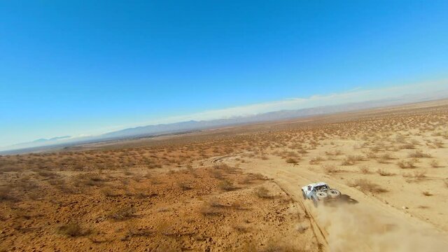 Off-road truck competing in a Mojave Desert rally speeds through the race course track followed by a first-person drone
