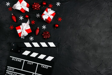 Movie clapper board with Christmas decorations and gifts on a black background with copy space.