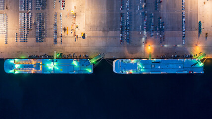New car lined up in the port for import export around the world, Automobile and automotive roro carrier boat vessel terminal, Aerial view rows of new car at night waiting to be dispatch and shipped.