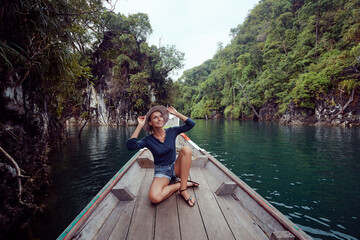 Fototapeta na wymiar Happy vacation in Thailand. Pretty young woman taking sailing Khao Sok National Park lake on traditional longtail boat.