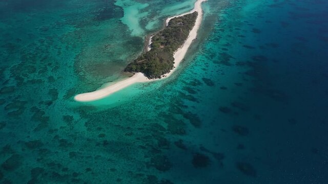 Nice and slow drone shot very high up, looking down on Cresta de Gallo Island in the Philippines with its white sand beaches, turquoise, green and blue water and coral reef around it in the sun.