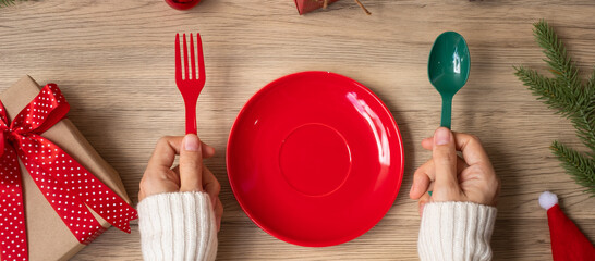 Merry Christmas with woman hand holding plate, fork and spoon on wood table background. Xmas, party...