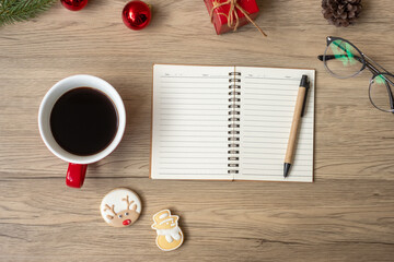 Blank notebook, black coffee cup, Christmas cookies and pen on wood table, Top view and copy space. Xmas, Happy New Year, Goals, Resolution, To do list, Strategy and Plan concept